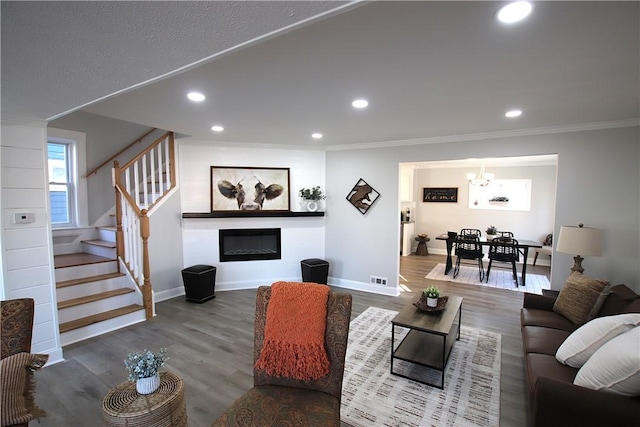 living room with stairs, a glass covered fireplace, crown molding, and wood finished floors