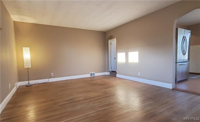 unfurnished living room featuring arched walkways, visible vents, baseboards, and wood finished floors