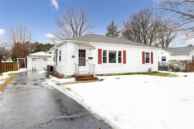 view of front facade with a detached garage, fence, central AC unit, an outbuilding, and driveway