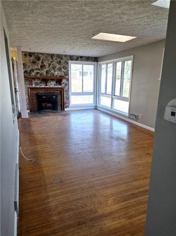 unfurnished living room with a skylight, baseboards, a textured ceiling, and wood finished floors