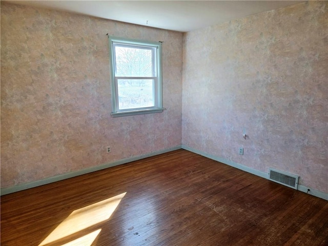 spare room with wood finished floors, visible vents, and baseboards