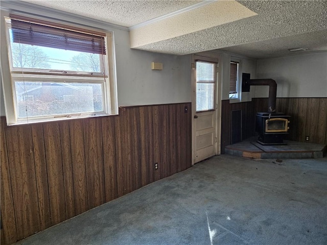 interior space with wooden walls, carpet flooring, wainscoting, a wood stove, and a textured ceiling