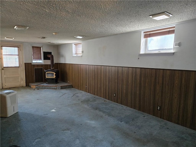 below grade area with carpet, a wainscoted wall, wood walls, a wood stove, and a textured ceiling