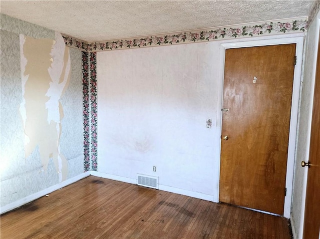 unfurnished room featuring visible vents, baseboards, a textured ceiling, and wood finished floors