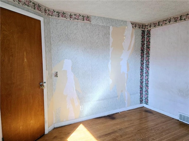 empty room with baseboards, wood finished floors, visible vents, and a textured ceiling