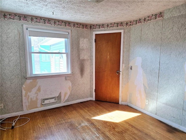 unfurnished room with visible vents, baseboards, a textured ceiling, and hardwood / wood-style floors