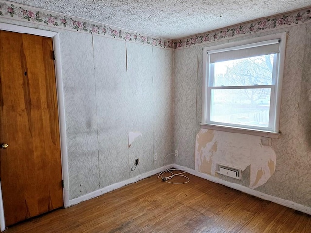 unfurnished room with baseboards, a textured ceiling, and wood finished floors