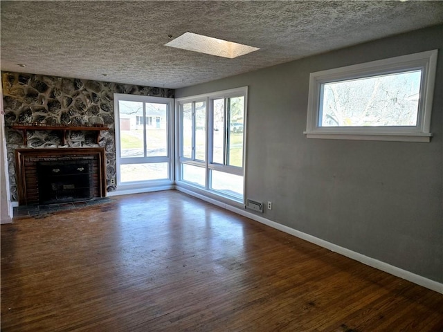 unfurnished living room with a stone fireplace, wood finished floors, a wealth of natural light, and a textured ceiling