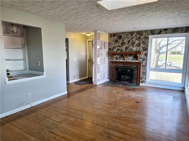 unfurnished living room with a textured ceiling, wood finished floors, baseboards, and a large fireplace