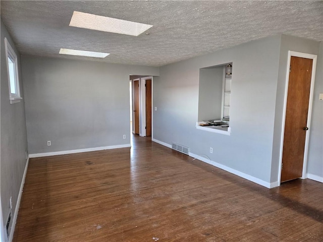 unfurnished room featuring visible vents, a skylight, baseboards, and wood finished floors