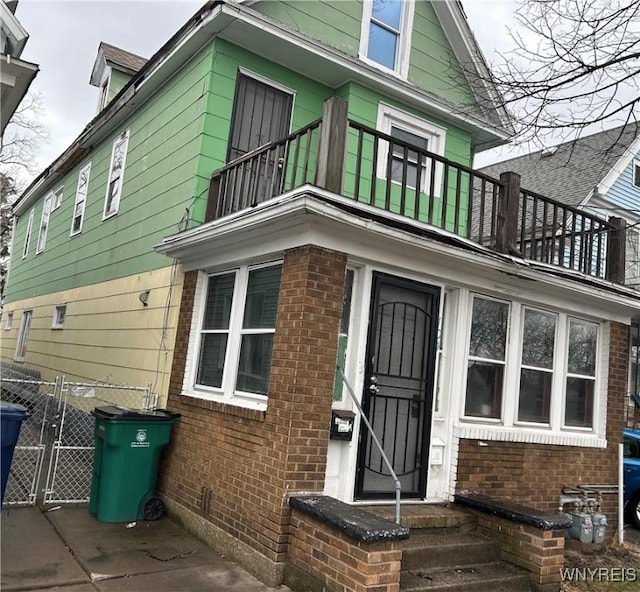 view of front of property with fence, brick siding, a balcony, and a gate