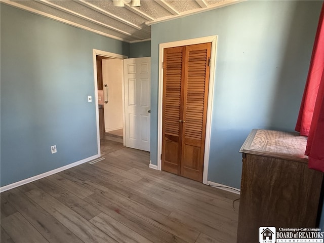 unfurnished bedroom featuring wood finished floors, a closet, and baseboards