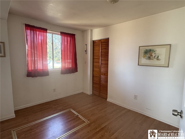 unfurnished bedroom featuring wood finished floors, a closet, and baseboards