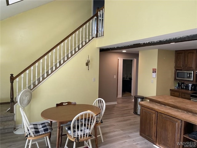 dining space with stairs, baseboards, light wood-type flooring, and a towering ceiling