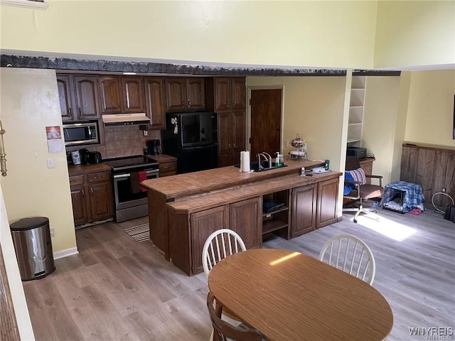 kitchen featuring under cabinet range hood, dark brown cabinets, appliances with stainless steel finishes, and light wood-type flooring