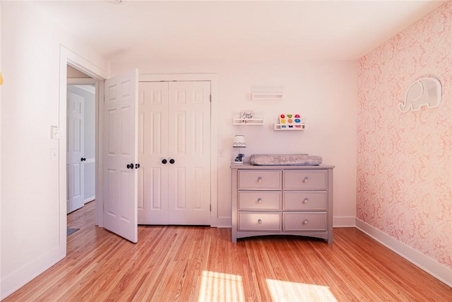 unfurnished bedroom with light wood-type flooring, baseboards, a closet, and wallpapered walls