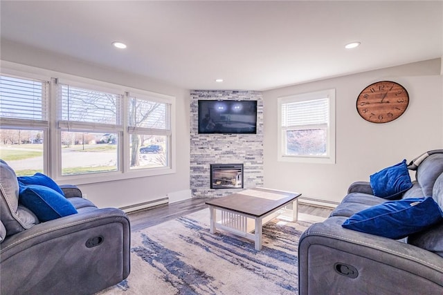 living area with baseboards, baseboard heating, recessed lighting, a stone fireplace, and wood finished floors