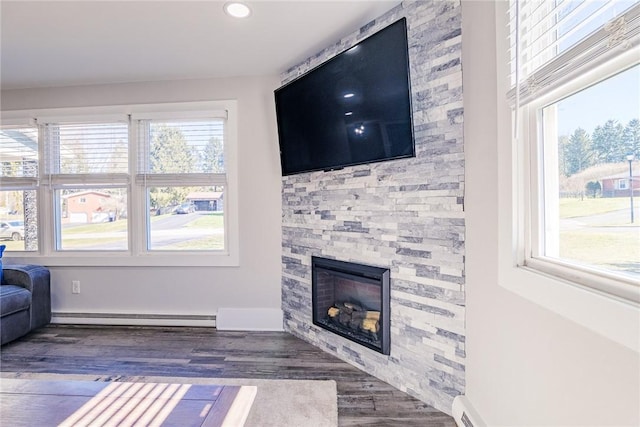 living room with a wealth of natural light, baseboard heating, wood finished floors, and a fireplace