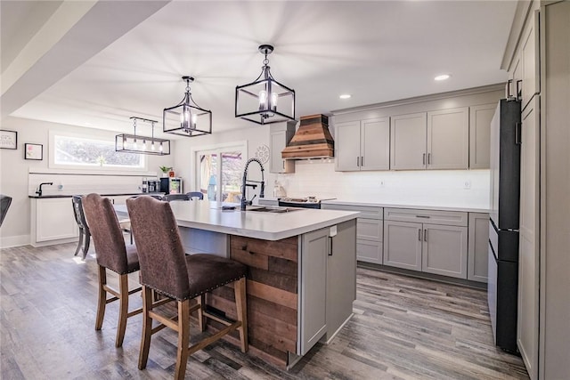 kitchen with backsplash, gray cabinets, freestanding refrigerator, custom exhaust hood, and a sink