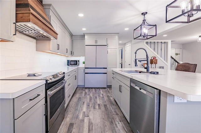 kitchen with light wood-style flooring, a sink, light countertops, custom range hood, and appliances with stainless steel finishes