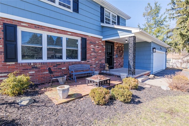 view of front of home featuring brick siding, an attached garage, and a patio area