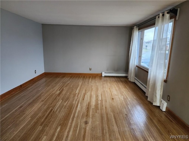 empty room featuring wood finished floors, baseboards, and a baseboard radiator