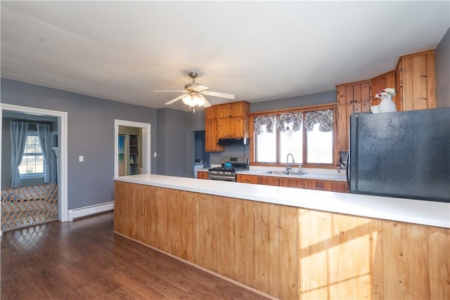 kitchen with a sink, freestanding refrigerator, stainless steel range with gas cooktop, light countertops, and baseboard heating