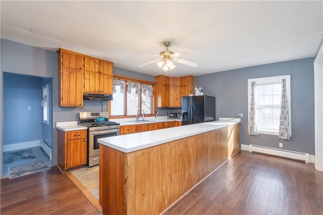 kitchen featuring a sink, a baseboard heating unit, stainless steel appliances, brown cabinetry, and light countertops