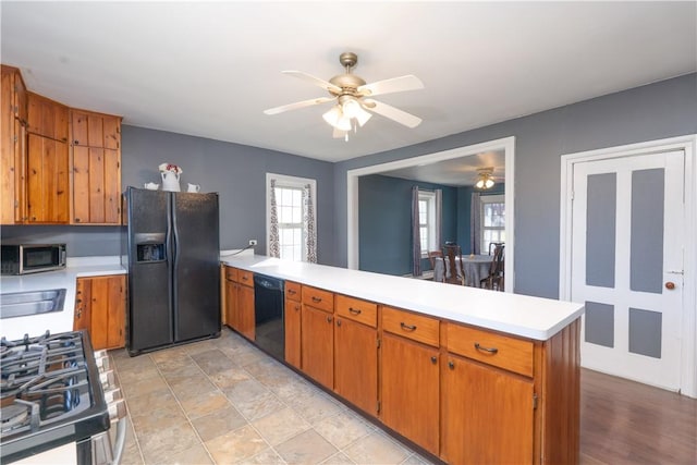 kitchen featuring light countertops, brown cabinets, a peninsula, black appliances, and a ceiling fan