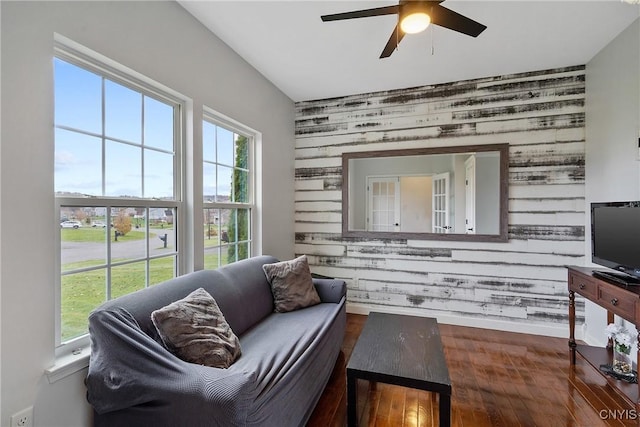 living room with ceiling fan, plenty of natural light, wooden walls, and wood finished floors