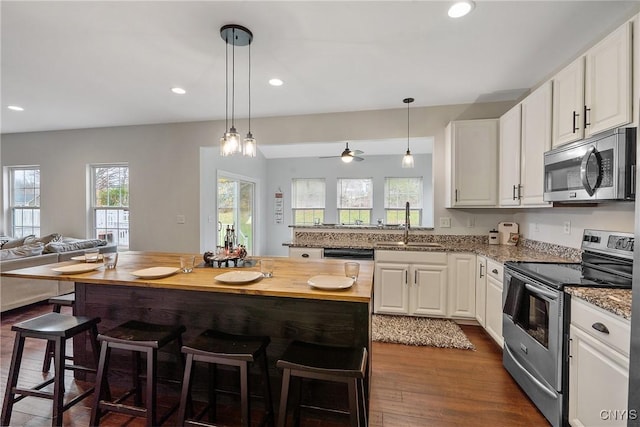 kitchen with dark wood-type flooring, open floor plan, appliances with stainless steel finishes, white cabinetry, and a sink