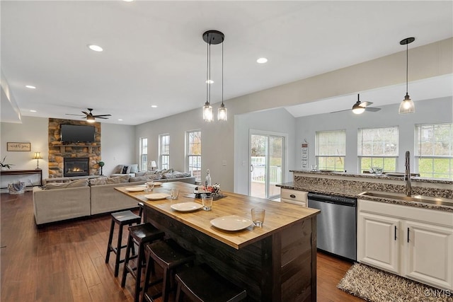 kitchen with a sink, white cabinetry, a stone fireplace, dishwasher, and hanging light fixtures