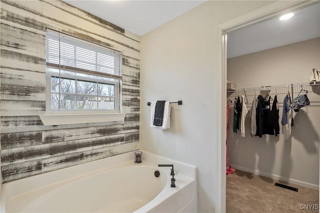 full bath with a walk in closet, a garden tub, baseboards, and visible vents