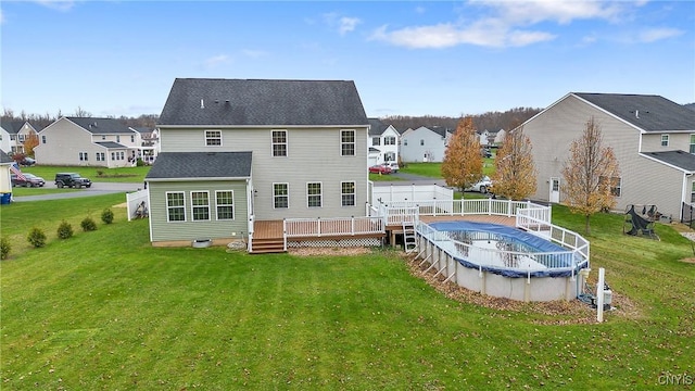 back of property with a covered pool, a residential view, a lawn, and a wooden deck