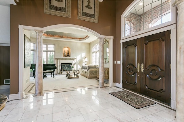 entryway featuring baseboards, visible vents, ornate columns, a glass covered fireplace, and a raised ceiling