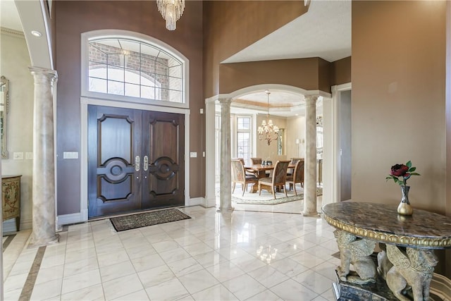 entryway featuring baseboards, a chandelier, a towering ceiling, arched walkways, and ornate columns