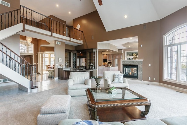 carpeted living room with visible vents, baseboards, a multi sided fireplace, stairway, and a towering ceiling