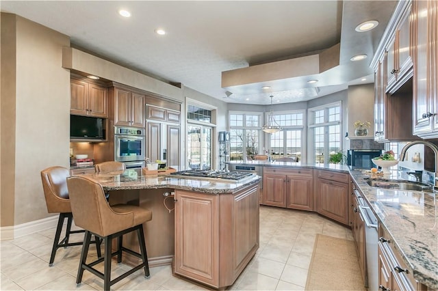 kitchen featuring a kitchen bar, a sink, a kitchen island, stainless steel appliances, and light stone countertops