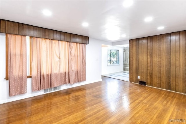 empty room with recessed lighting, wood finished floors, visible vents, and wood walls