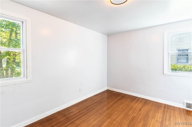 spare room with wood finished floors, a healthy amount of sunlight, baseboards, and visible vents