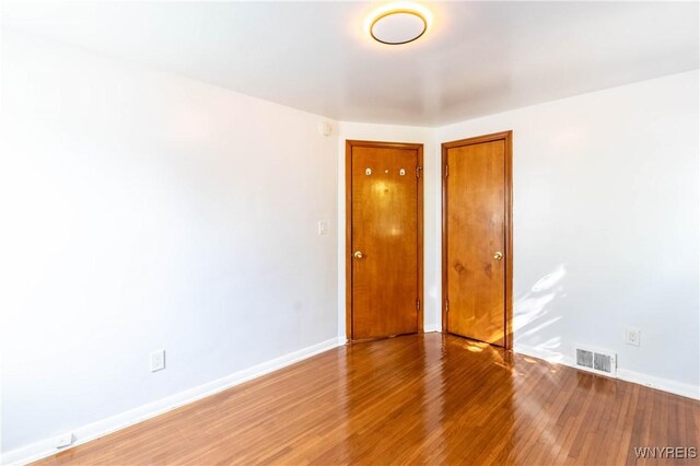 empty room with wood finished floors, visible vents, and baseboards