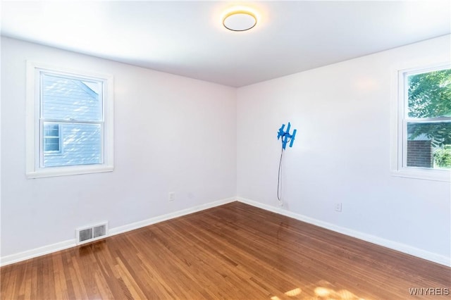 empty room featuring wood finished floors, visible vents, and baseboards