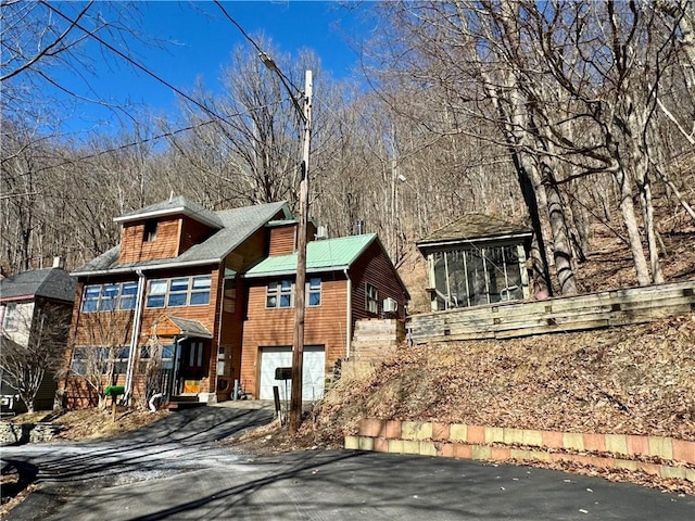 chalet / cabin featuring aphalt driveway, an attached garage, and a sunroom