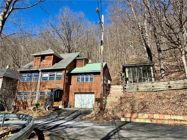 view of front of home with aphalt driveway, a garage, and a sunroom