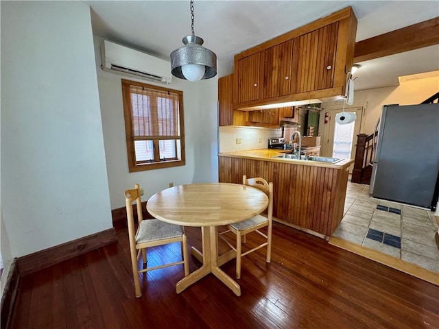 kitchen with a wall mounted air conditioner, decorative backsplash, freestanding refrigerator, brown cabinetry, and a sink