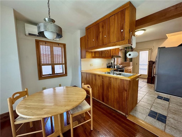 kitchen with tasteful backsplash, brown cabinets, a peninsula, freestanding refrigerator, and a sink