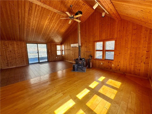 unfurnished living room featuring wooden walls, wood ceiling, a wood stove, high vaulted ceiling, and wood-type flooring