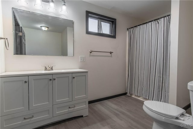 bathroom featuring curtained shower, baseboards, toilet, wood finished floors, and vanity