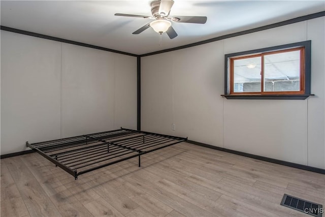 unfurnished bedroom featuring visible vents, ceiling fan, light wood-type flooring, ornamental molding, and a decorative wall