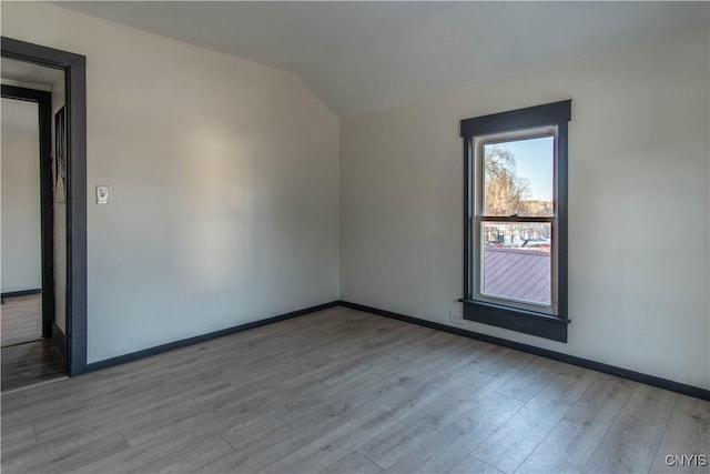 spare room with vaulted ceiling, baseboards, and wood finished floors